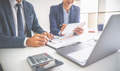 Image of two business professionals looking at papers with a laptop and calculator