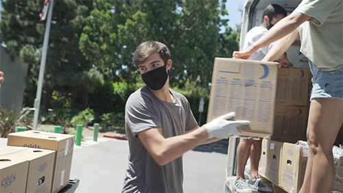 photo of a young man wearing a mask and glove moving aid boxes from a van to a pallet