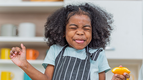 photo of a young girl making a sour taste face with an orange in her hand